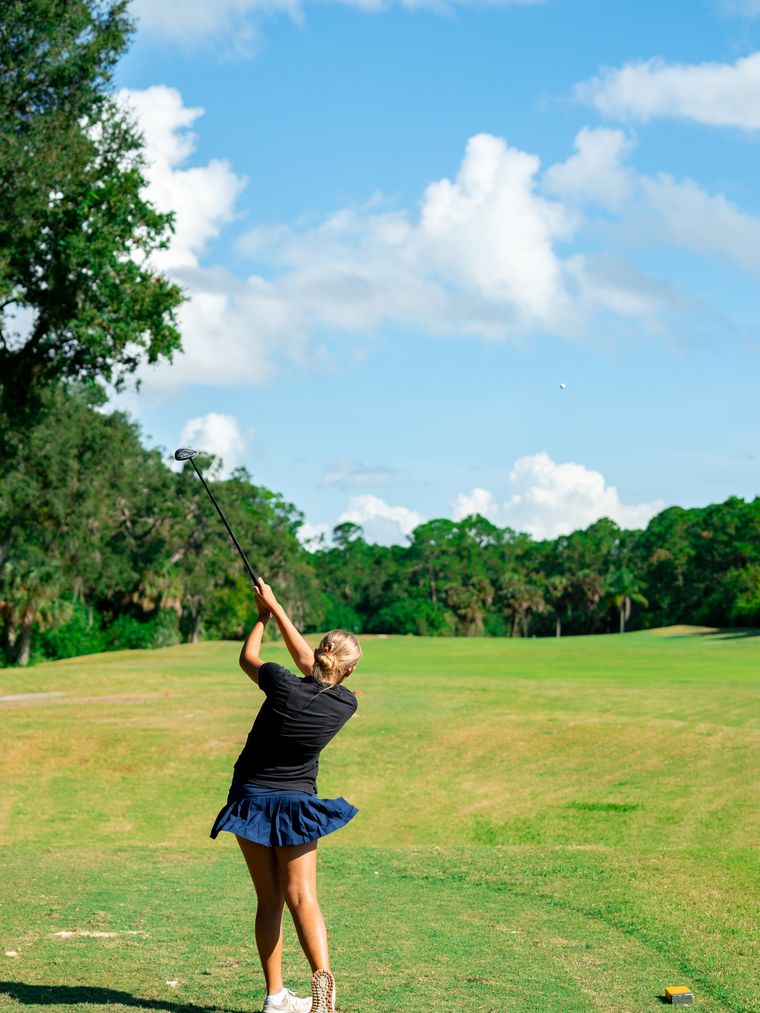 A DME golfer at the finish of a full swing under open sky.