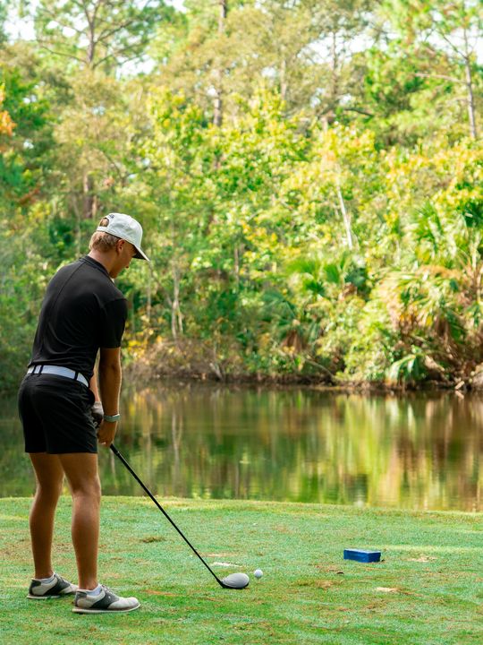 A DME golfer standing over a shot beside the water, working through a pre-shot routine.