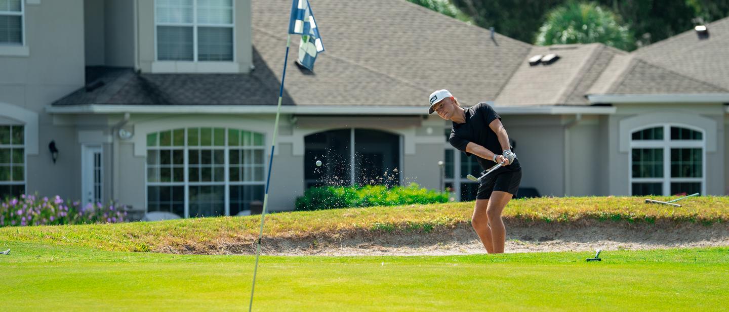A DME Academy golfer playing a greenside bunker shot during a round.
