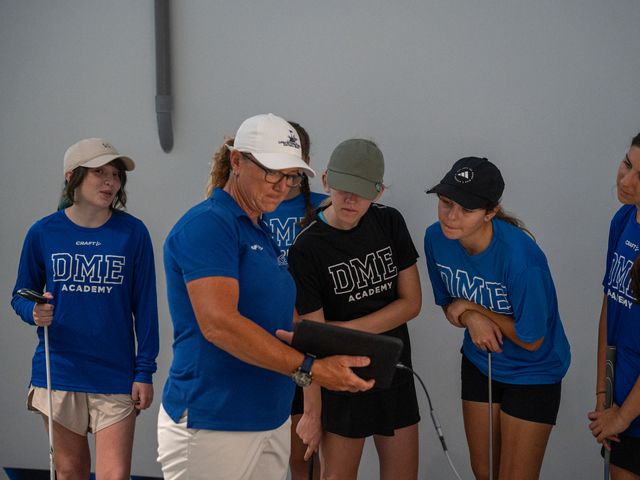 A DME coach reviewing performance footage on a tablet with a group of golfers.