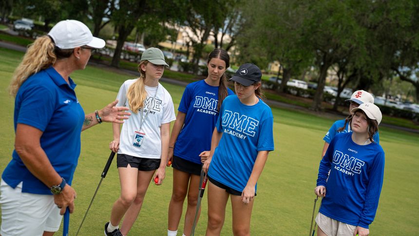 A DME coach walking a hole with a group of golfers.