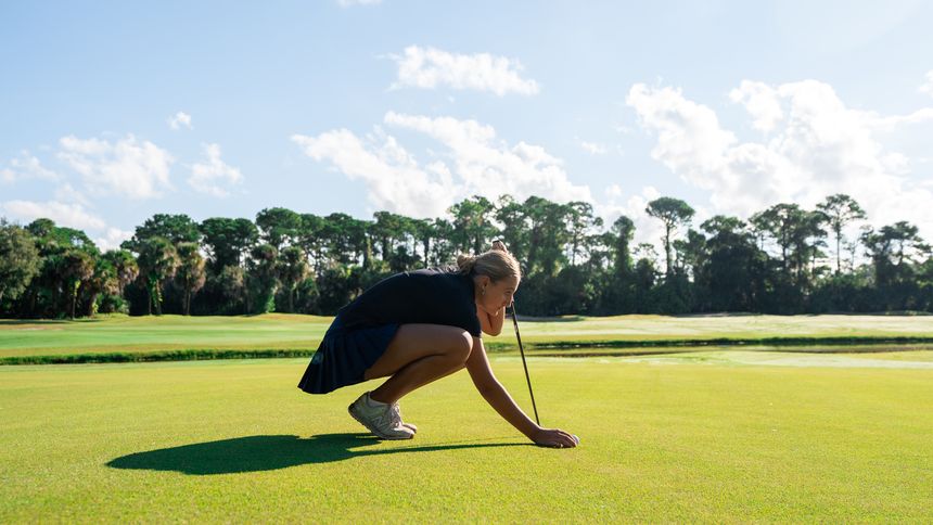 A DME golfer crouching to read the line of a putt.