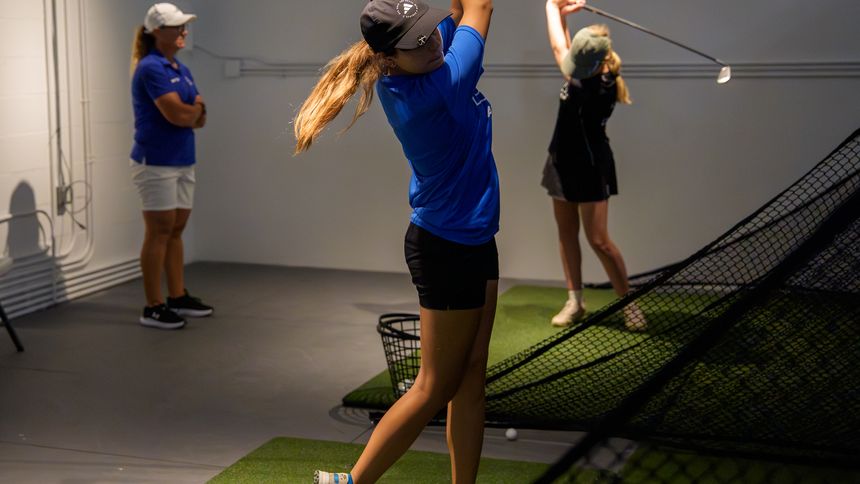 DME golfers working through swings in the academy's indoor training bay.