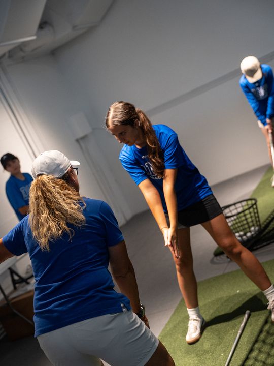 A DME coach working through swing mechanics with golfers in the indoor bay.